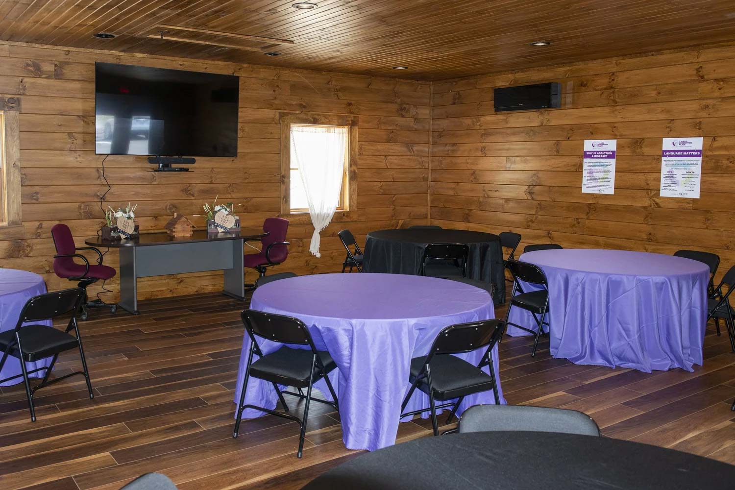 Room with wooden walls and circular tables arranged throughout.