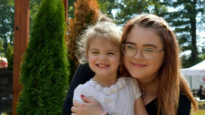 Young woman posing with her daughter, both of them smiling.
