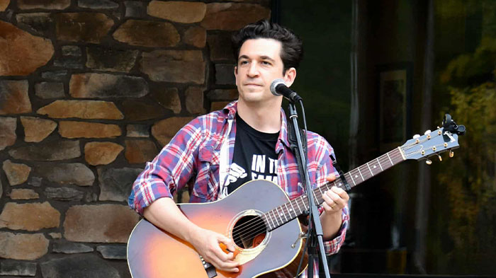 Man singing and playing acoustic guitar in front of a microphone.