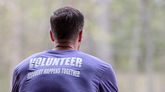 View of a man's back with his shirt reading "Volunteer: Recovery Happens Together"